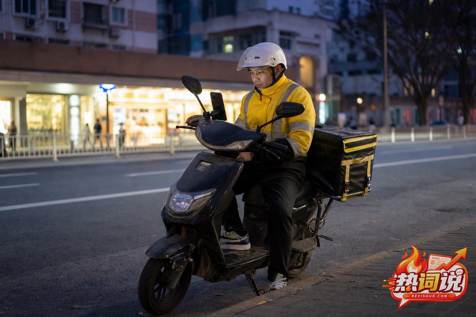 傍晚城市道路旁,一名戴好头盔的外卖骑手停稳电动车查看手机并短暂休息