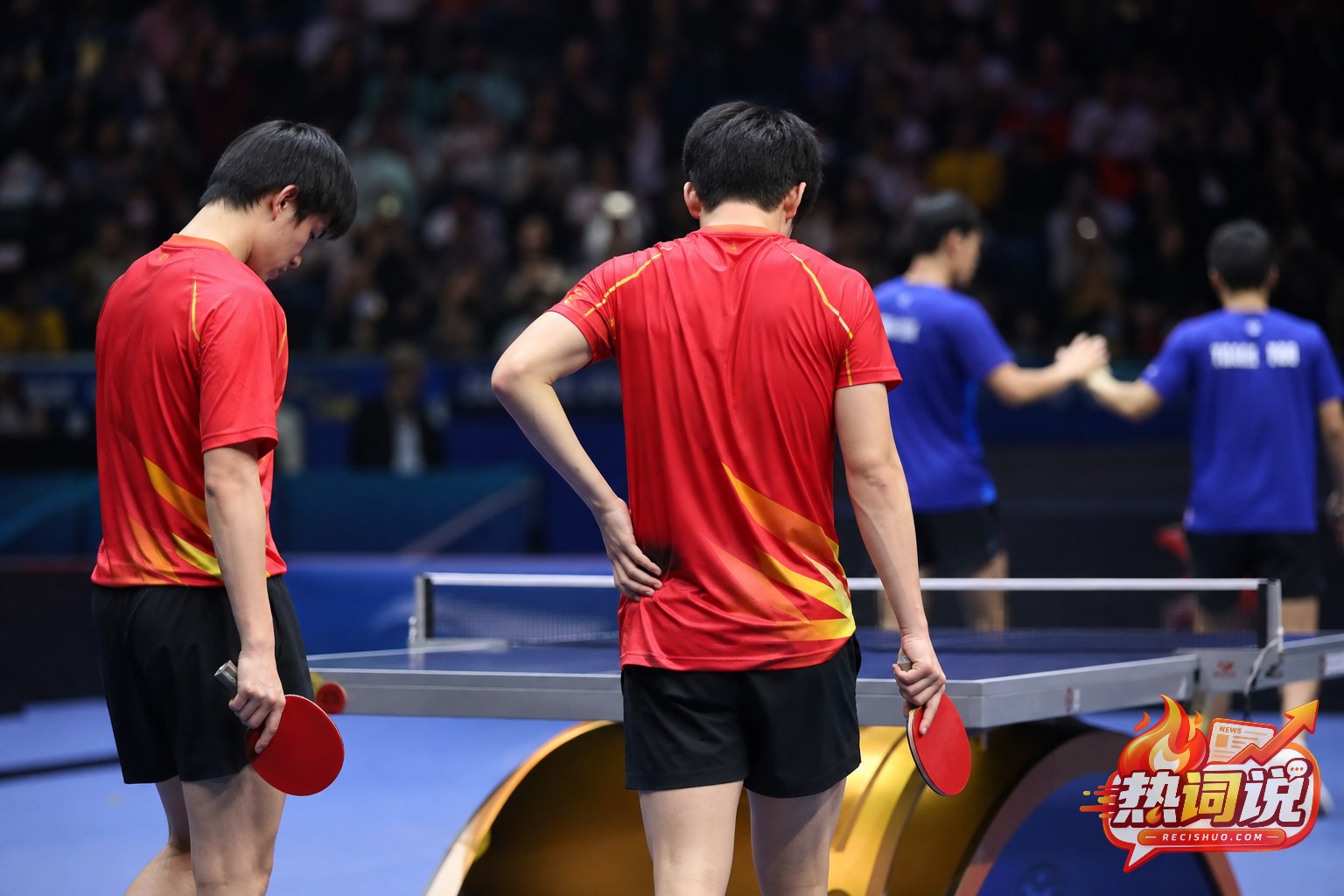 国际乒乓球赛后,两名身穿红色球衣的男双运动员在球台前低头整理情绪