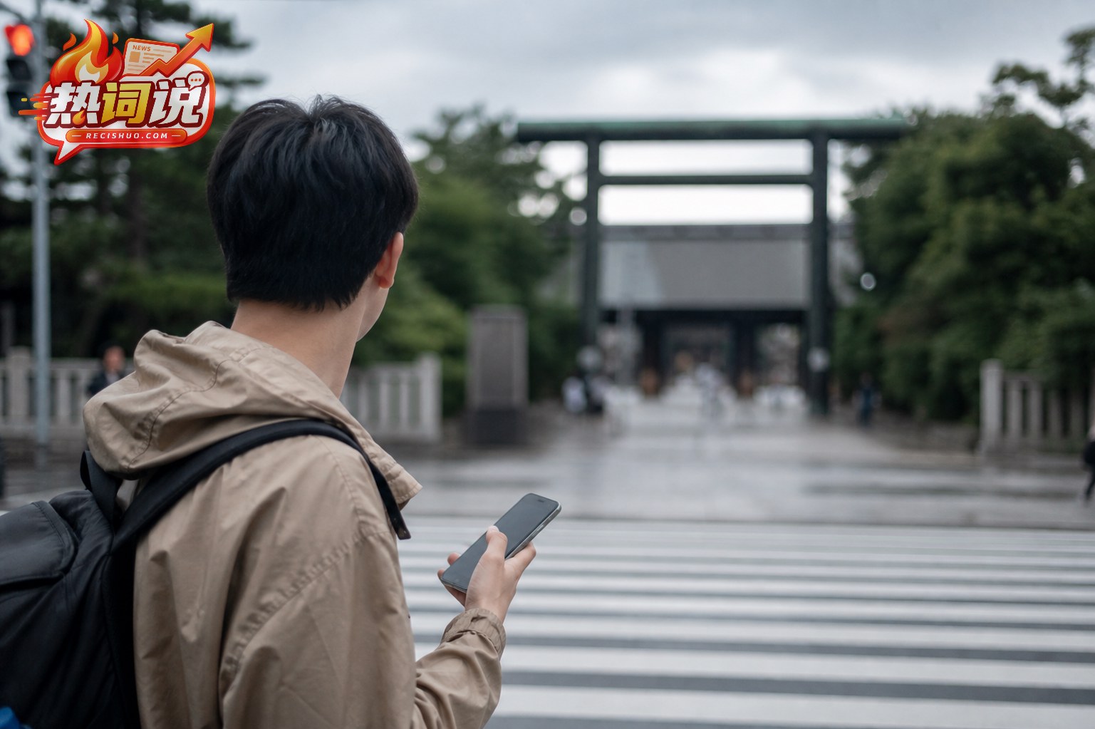 一名不露正脸的年轻旅行者手持手机,在阴天的东京街头望向远处的日式神社入口