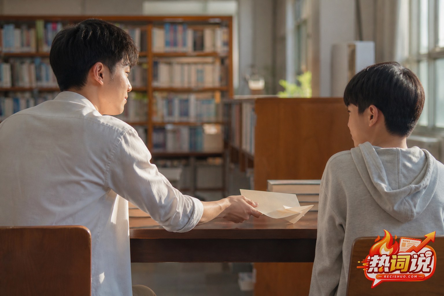 阳光下的图书馆内,一名青年把信纸和纸飞机递给少年