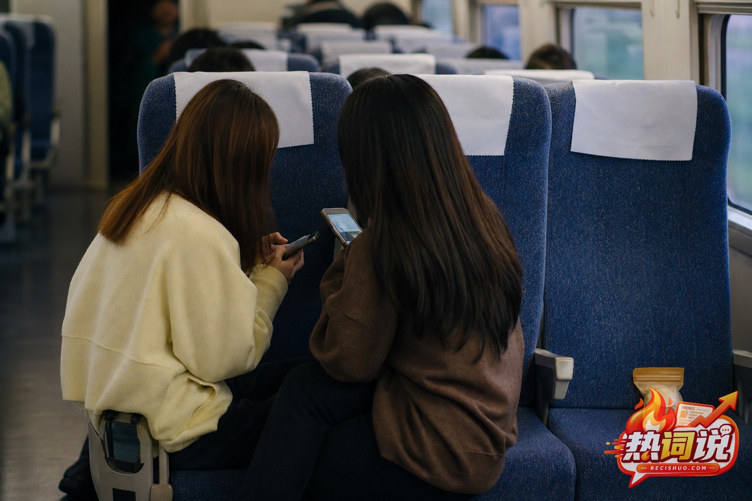 列车车厢内两名旅客坐在相邻座位上,旁边空座放有一袋零食