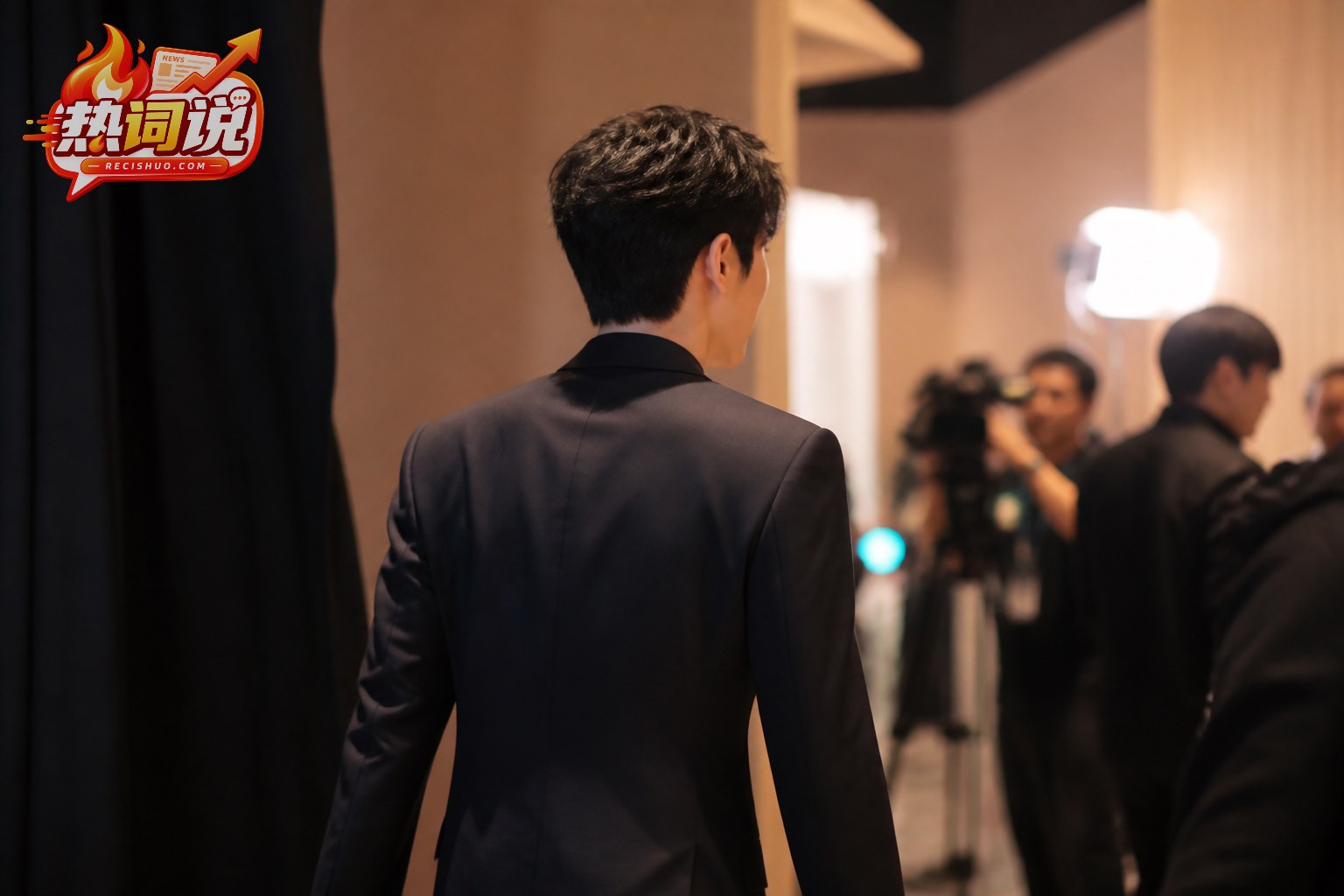 年轻男演员身穿深色西装从活动后台走向采访区的纪实场景