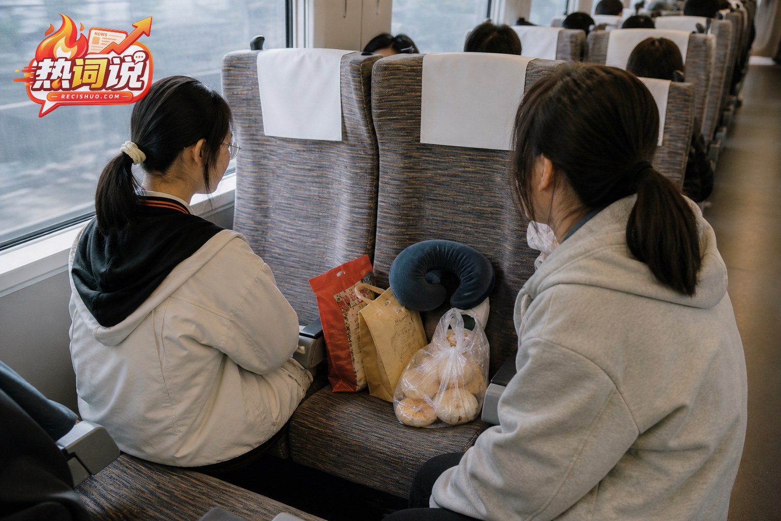 高铁车厢内两名女孩坐在相邻座位旁,空座上放有零食和旅行枕