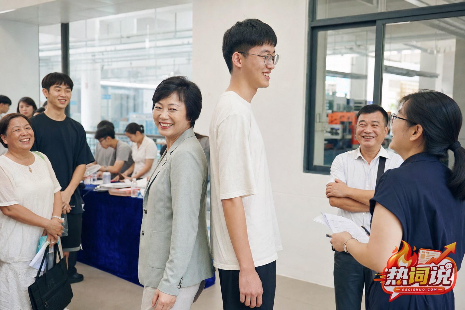 职业学校报名现场,短发女性管理者与一名高个男生背靠背比身高,家长和教师在旁微笑