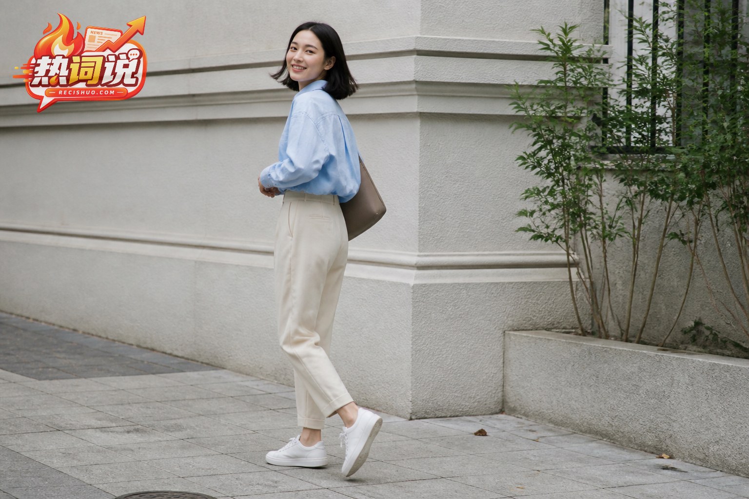 女性穿燕麦色锥形裤与浅蓝衬衫在城市街角转身抓拍