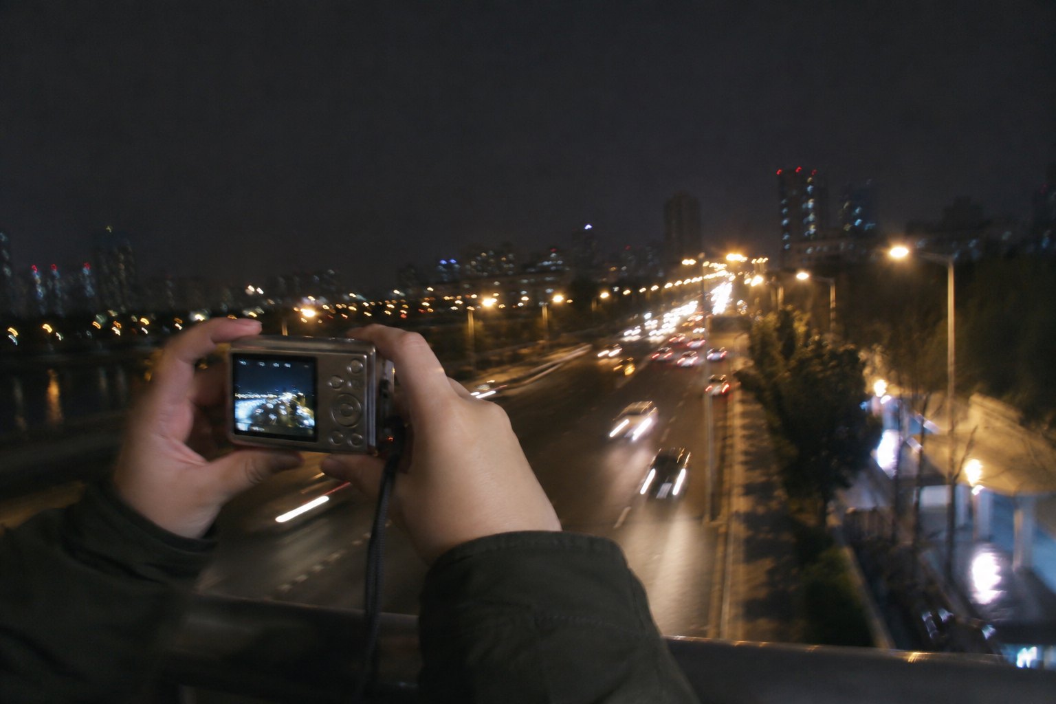 双手持便携数码相机拍摄夜间道路，路灯和车灯留下轻微光轨