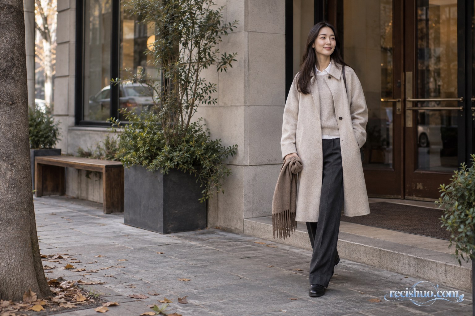 身穿燕麦色中长外套、薄针织与深色直筒裤的女性走在秋日街头