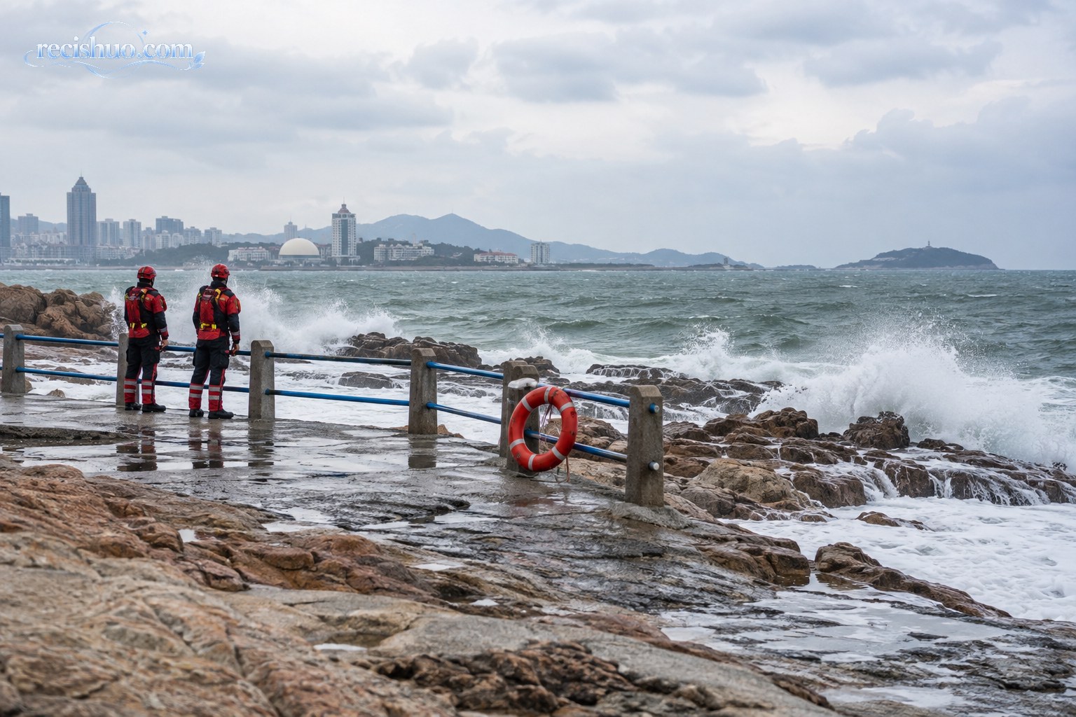 风浪较大的海岸边,两名救援人员隔着护栏观察海况,岸边设有救生圈
