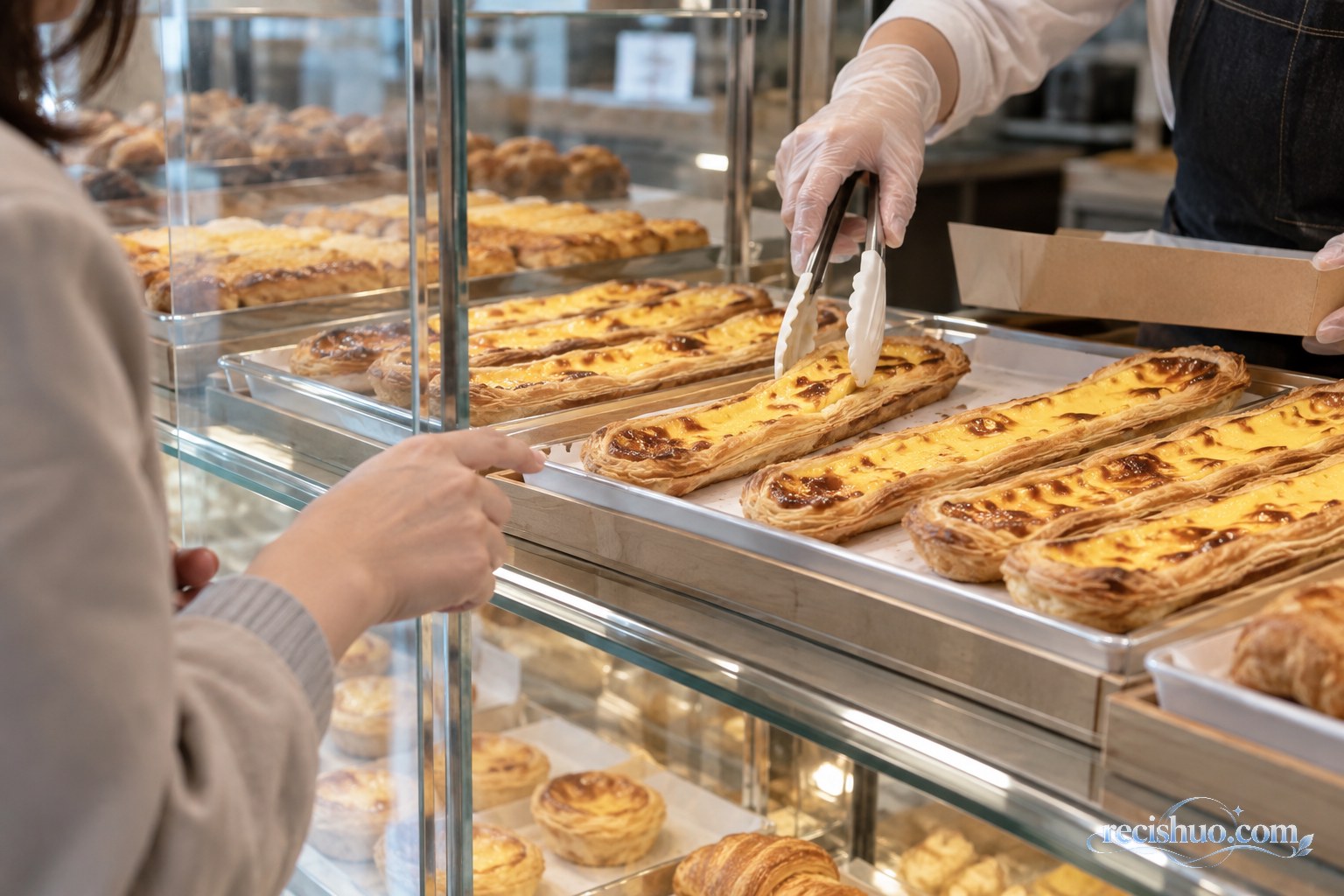 顾客在烘焙店展示柜前观察超长蛋挞并由店员用食品夹取餐