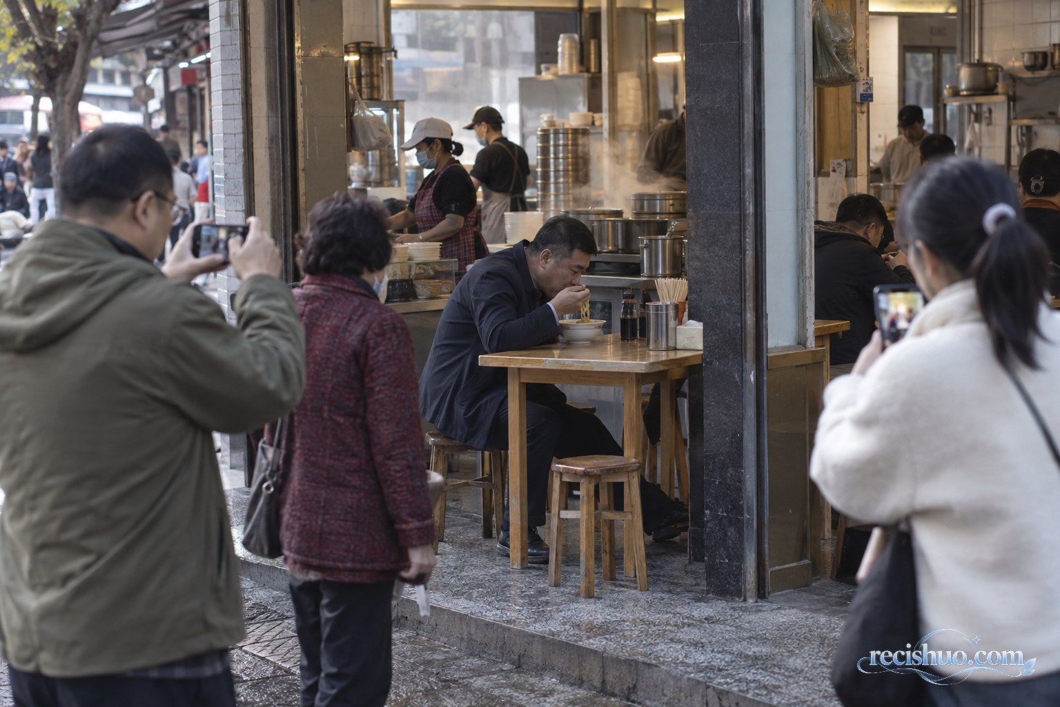 街坊早餐铺里一名男子正在吃面，几位路人在店外用手机记录