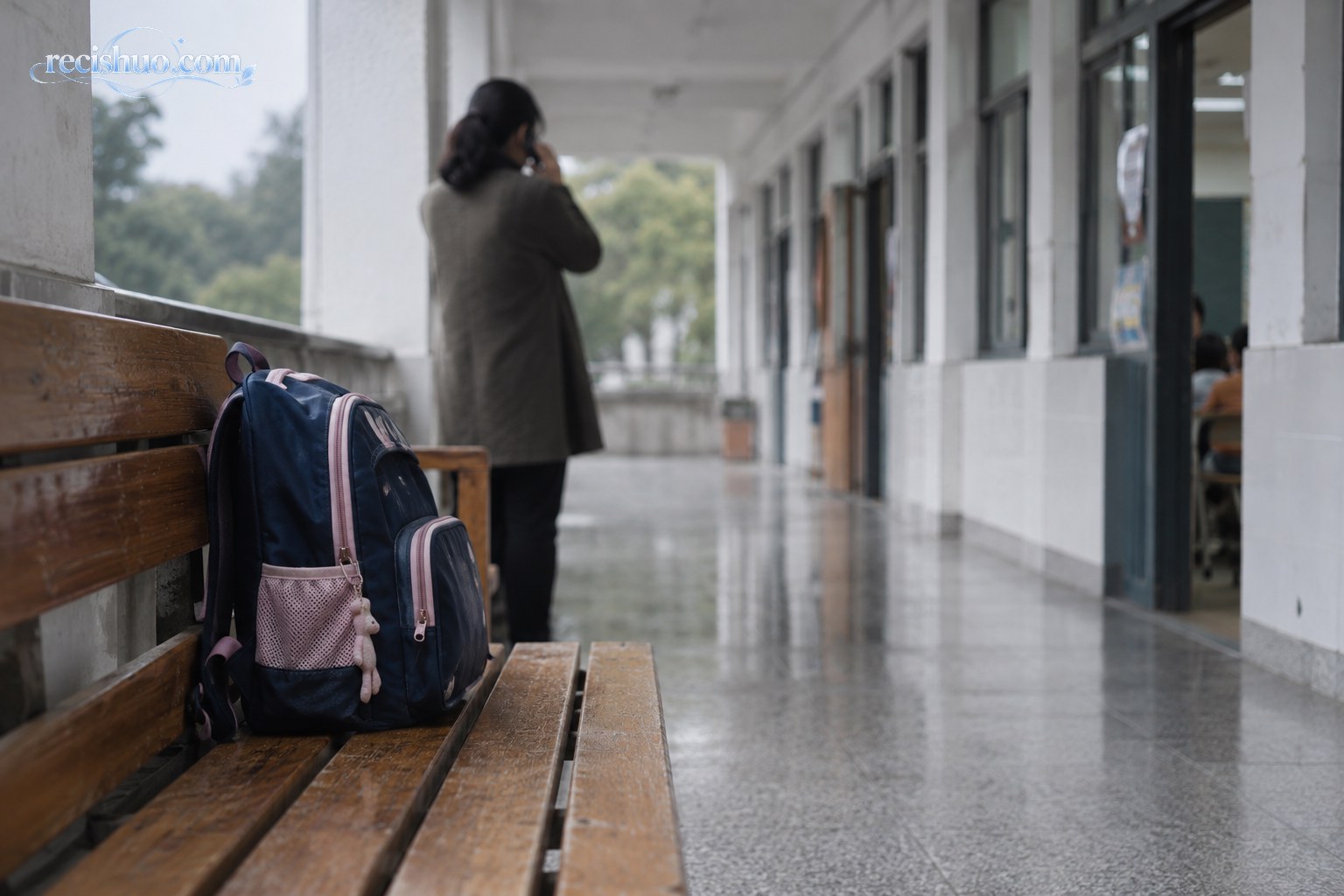 安静的小学校园走廊内,长椅上放着儿童书包,一名成年人在远处打电话求助