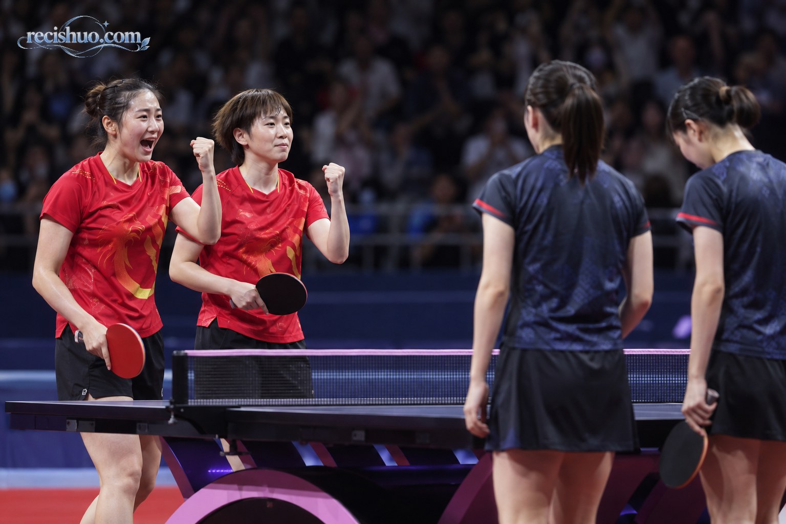 乒乓球女双比赛结束后两名红衣运动员在球台旁庆祝胜利