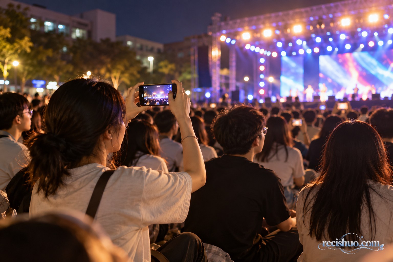 大学生在迎新晚会观众区观看演出并用手机记录舞台
