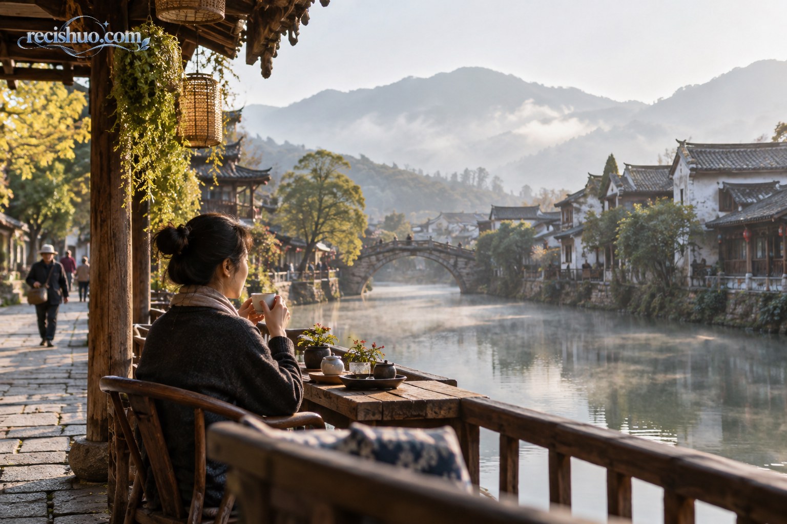 游客在云南古镇临水木廊边喝茶,晨雾笼罩远山与青瓦民居