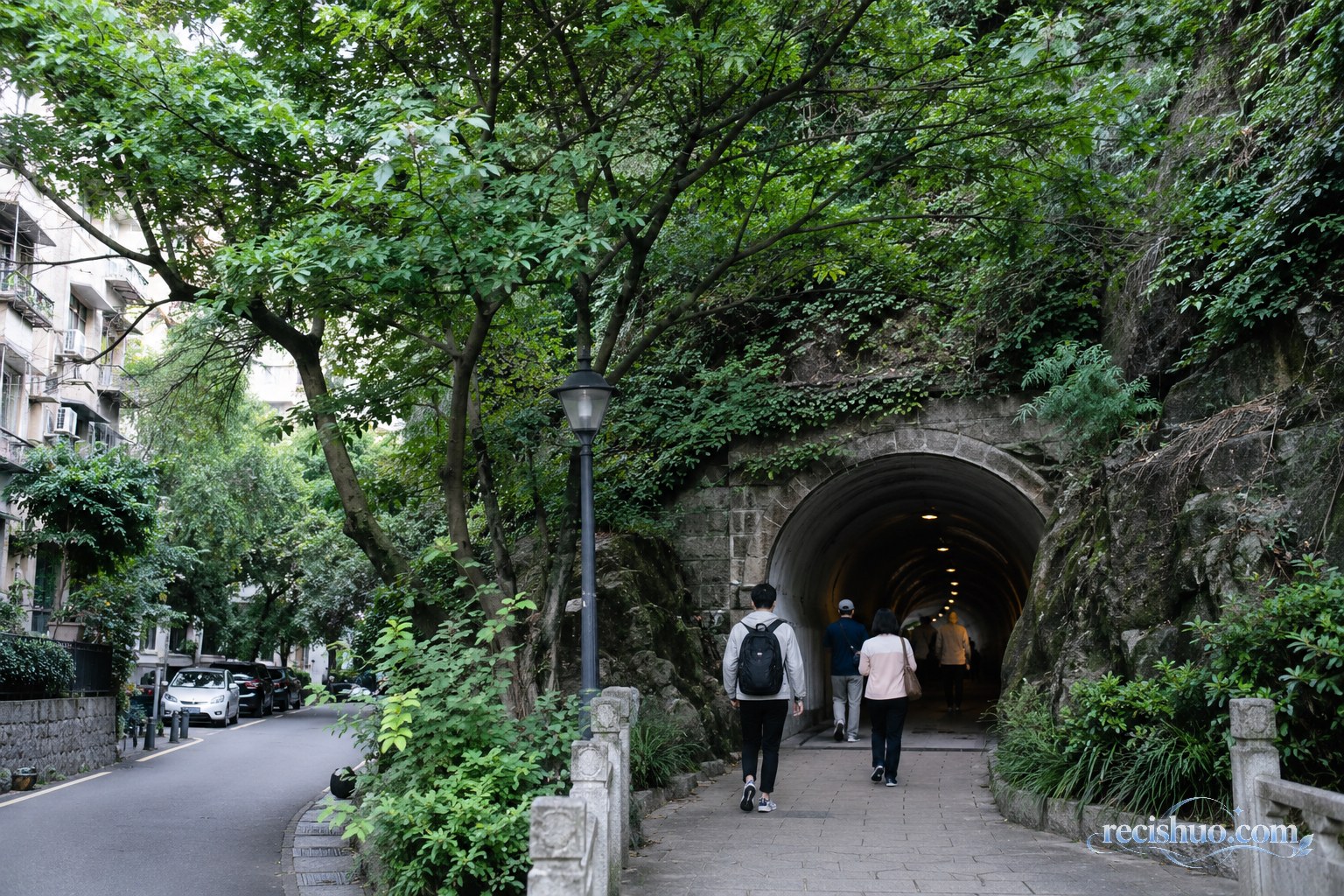 绿树与居民区之间一处城市山体步行隧道入口,行人正准备进入