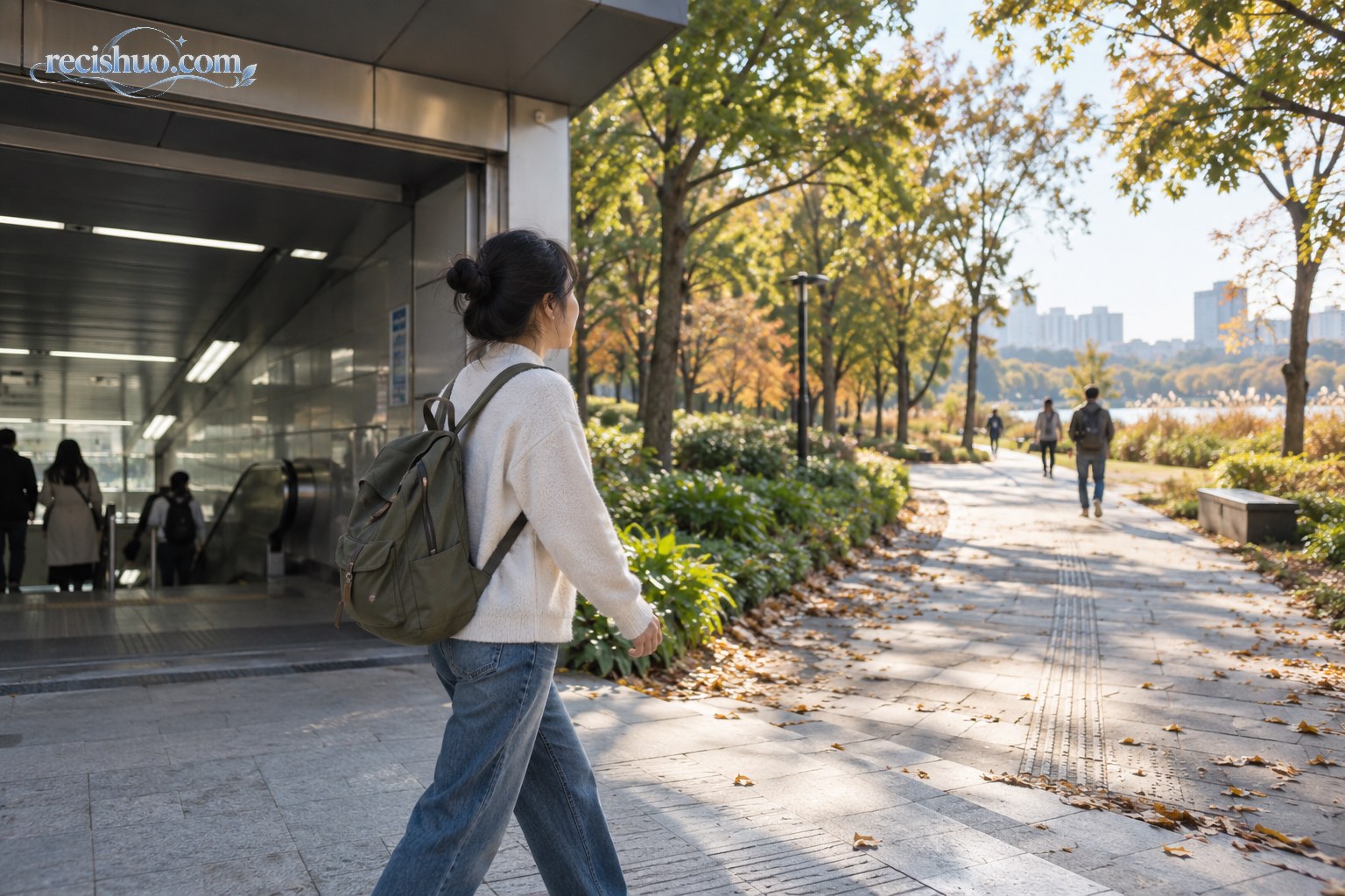 一名年轻人走出城市地铁口,迈向秋日阳光下的公园步道