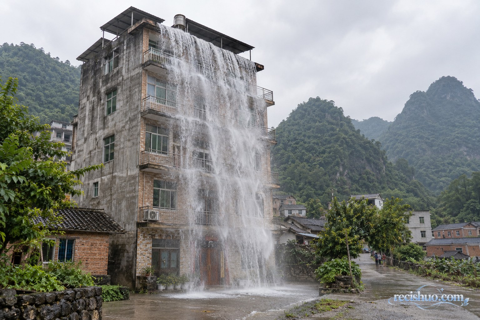 广西山村自建楼楼顶水流倾泻形成楼体瀑布的全景示意画面
