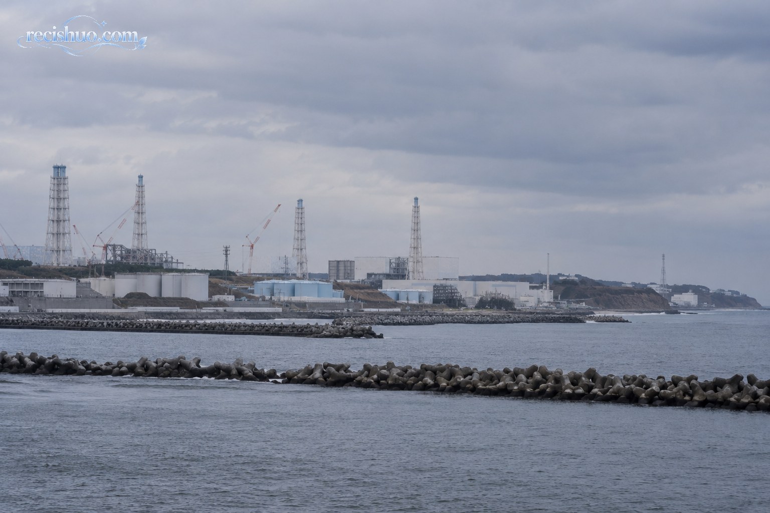 阴云下福岛沿岸海面、防波堤与远处临海工业设施的全景