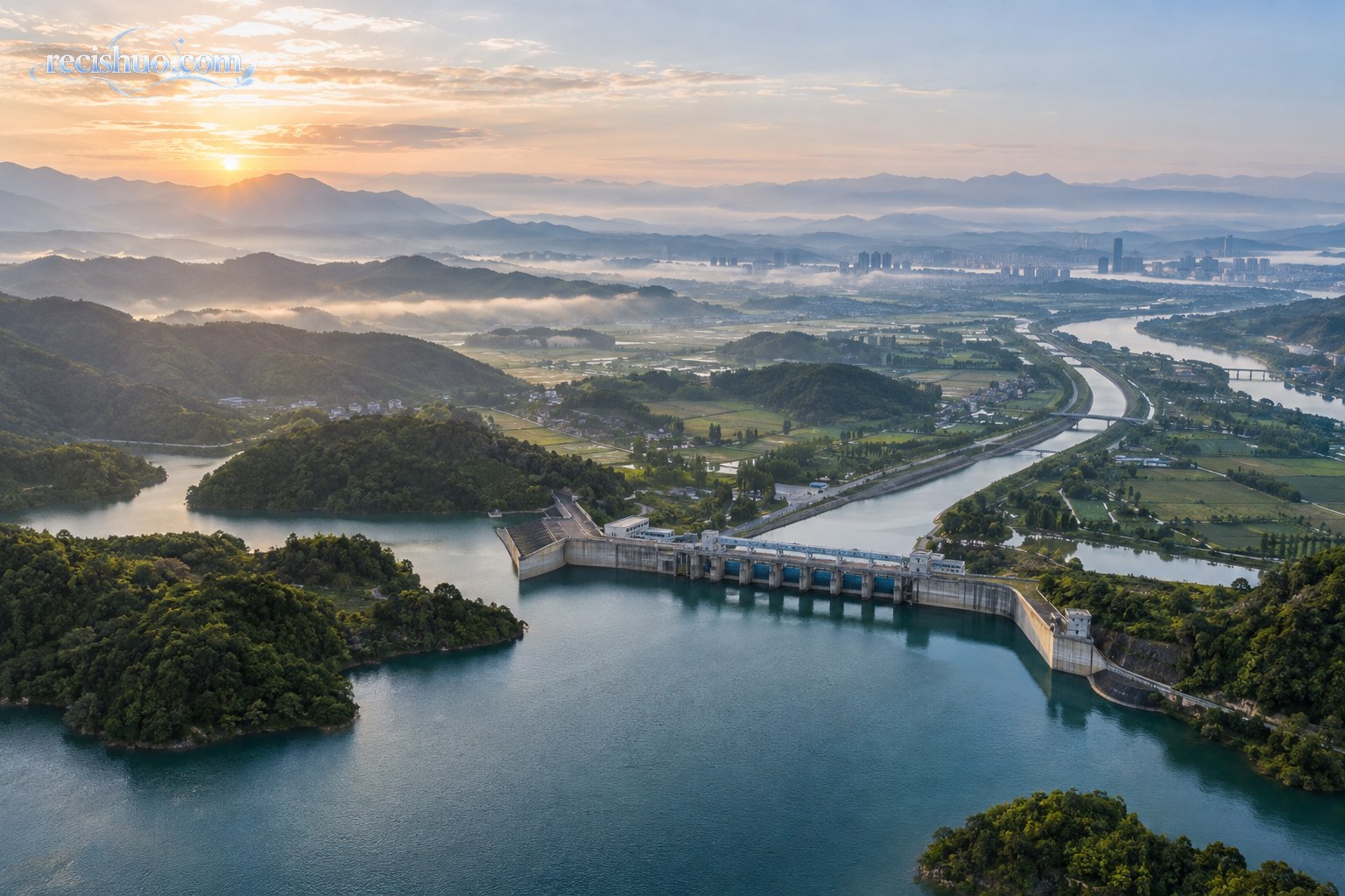 晨光下水库闸坝、输水渠道、河流、农田与远处城市相互连接的航拍景观