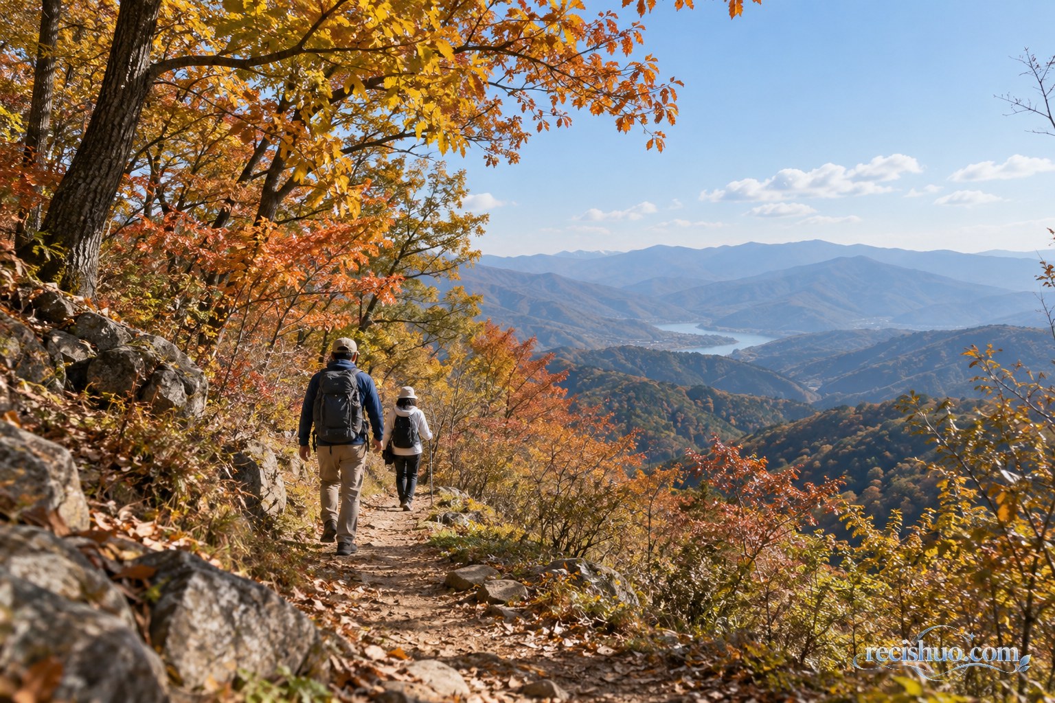 两名徒步者沿秋日山间步道前行,远处可见层叠山脊与湖泊