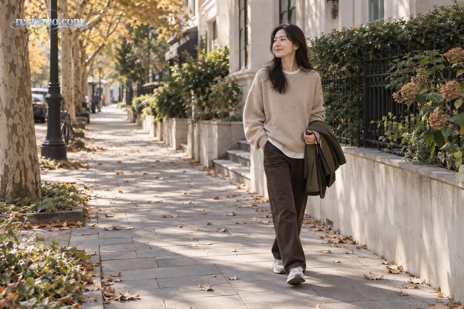 身穿燕麦色针织衫和深棕直筒裤的女性漫步在秋日街道