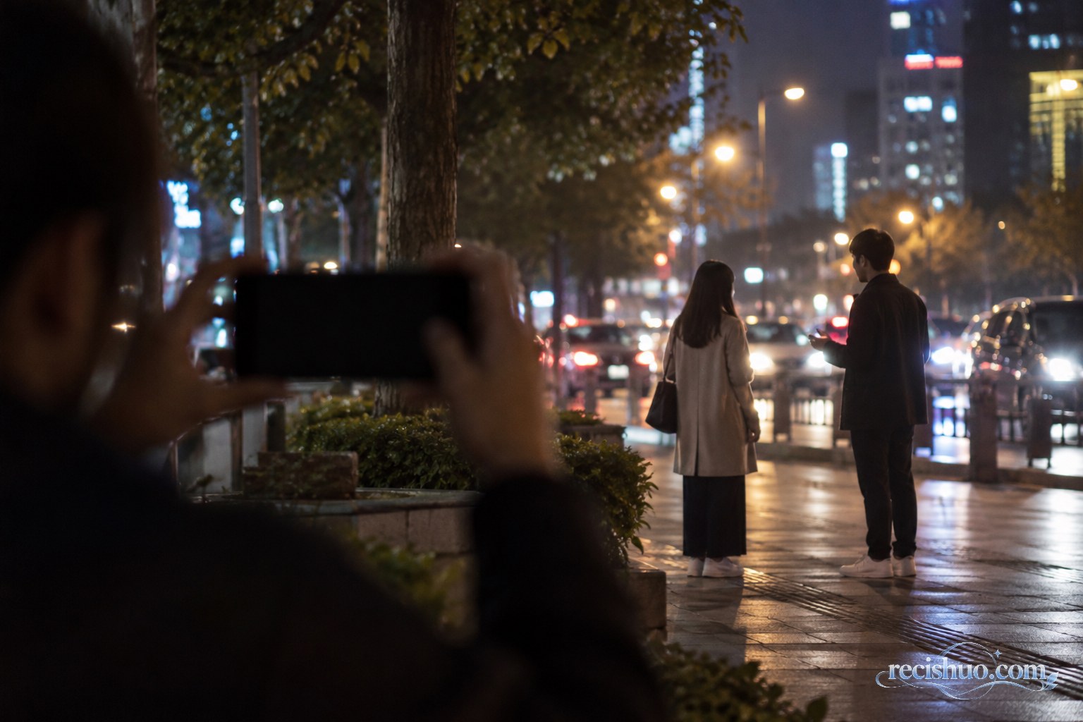夜晚城市街边一对男女交谈,近处有人用手机远距离拍摄
