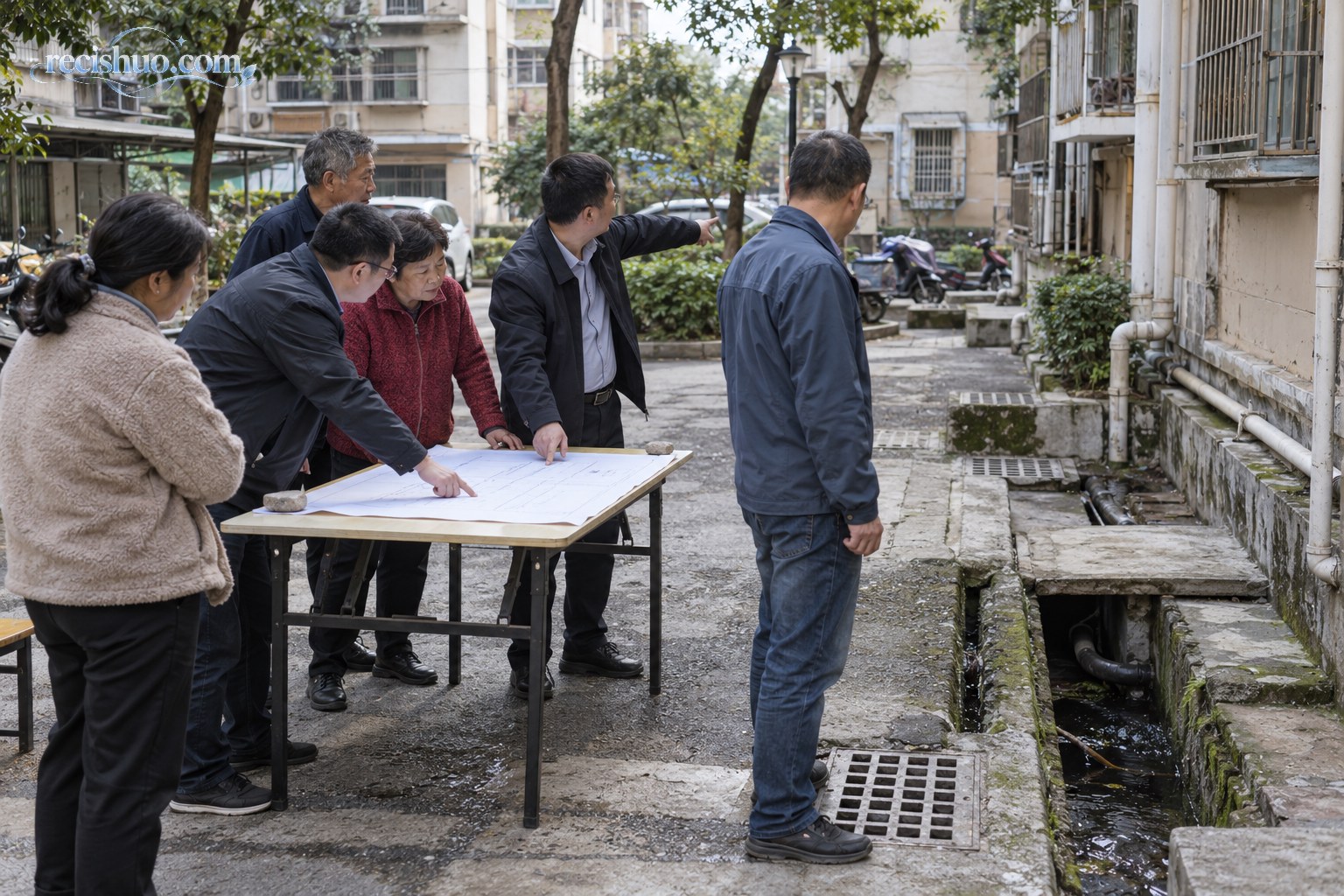 工作人员与居民在老旧小区现场围桌查看公共设施问题